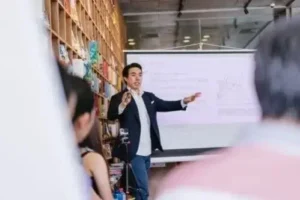 A man stands before a group, giving a presentation and interacting with attendees