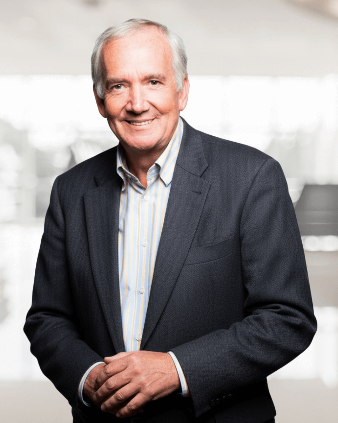 Elderly man in a dark suit and striped shirt smiles warmly, standing in a bright, blurred background. The tone is professional and approachable.